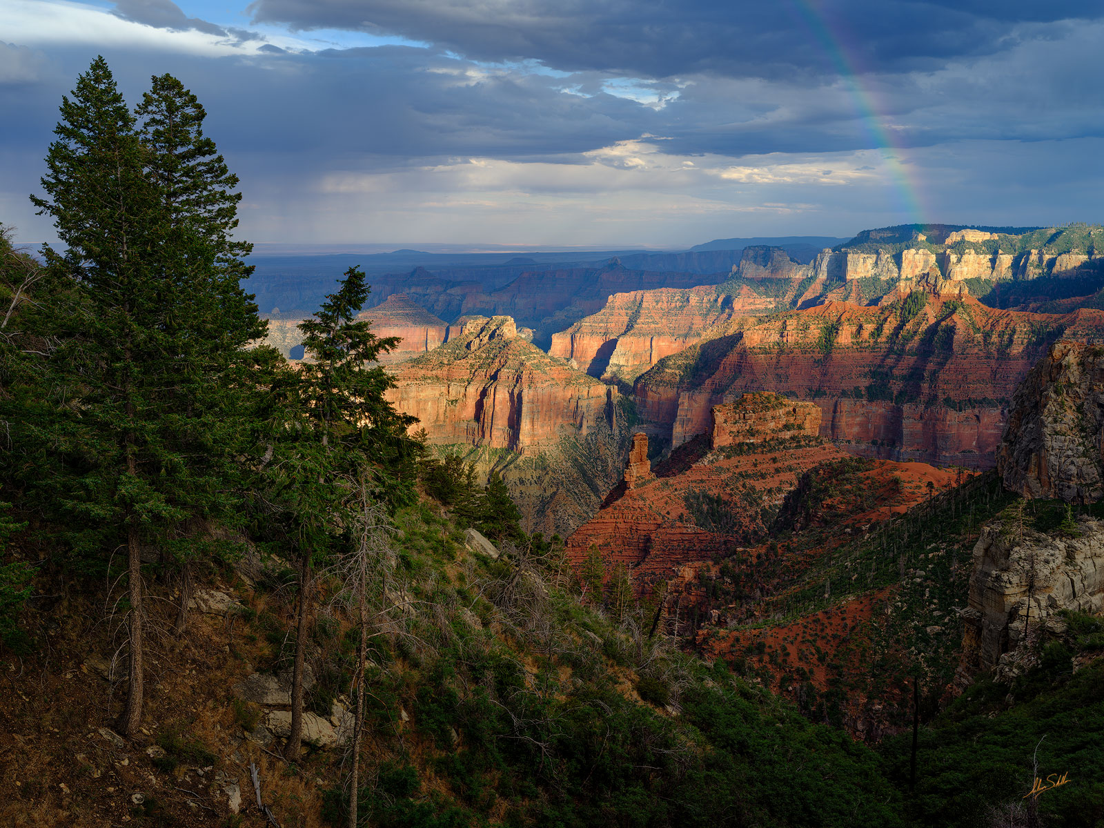 As a monsoon rain shower clears, light breaks through a gap in the clouds and a rainbow descends upon the Grand Canyon. From...